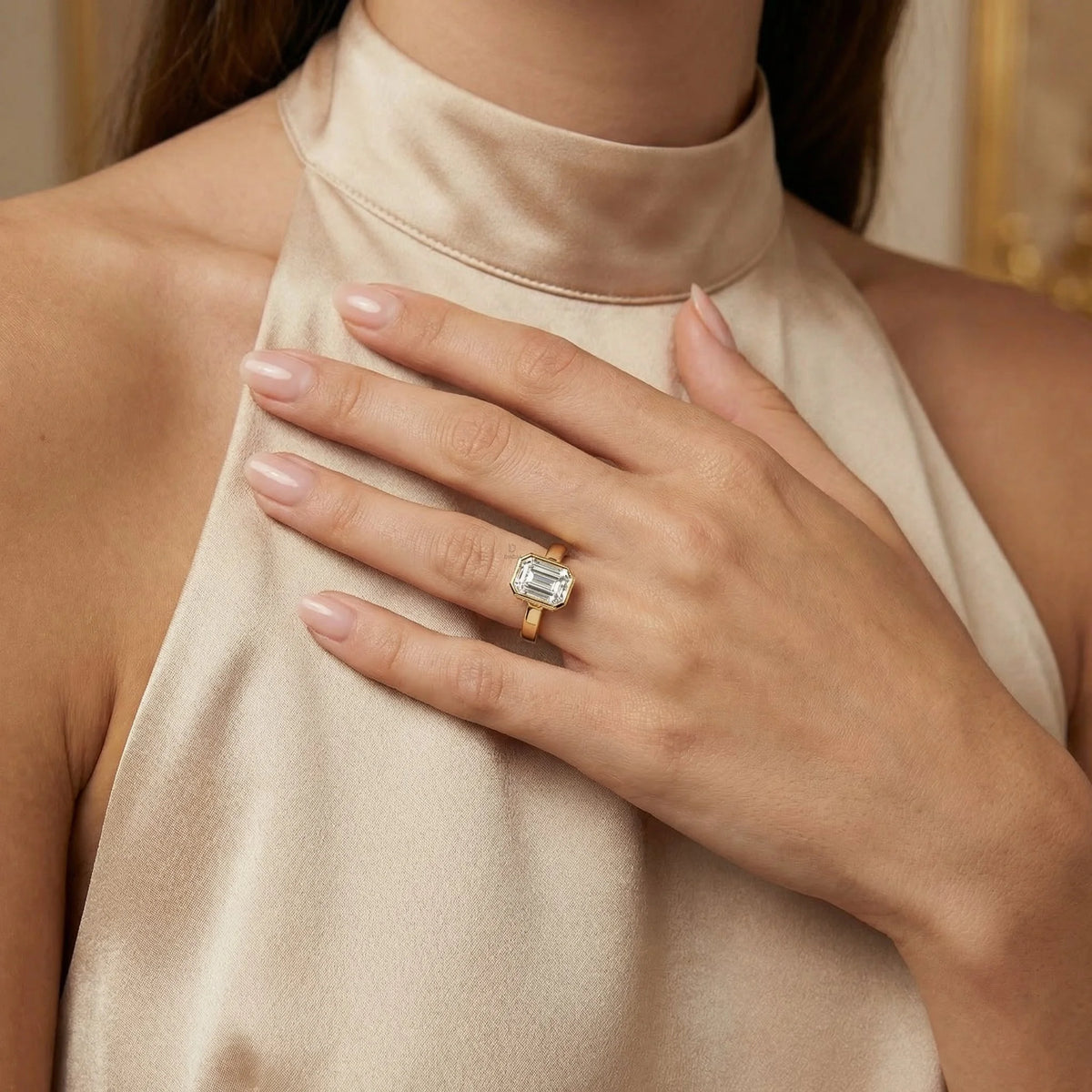 Woman wearing a yellow gold emerald-cut engagement ring with a bezel setting and hidden halo set pavé details ring.