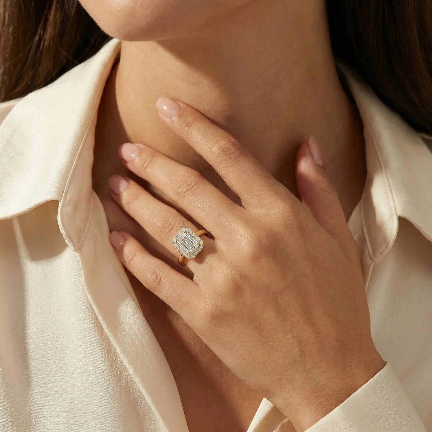 Elegant 14k yellow gold emerald cut diamond center stone engagement ring with a round cut halo setting band worn on a finger. A classic and luxurious jewelry piece displayed against soft silk.