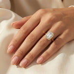 Elegant yellow gold emerald cut diamond engagement ring with a round cut halo setting band worn on a finger. A classic and luxurious jewelry piece displayed against soft silk.