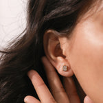 Close-up of a modern emerald cut diamond earring in a yellow gold bezel setting worn on a woman's ear piercing.