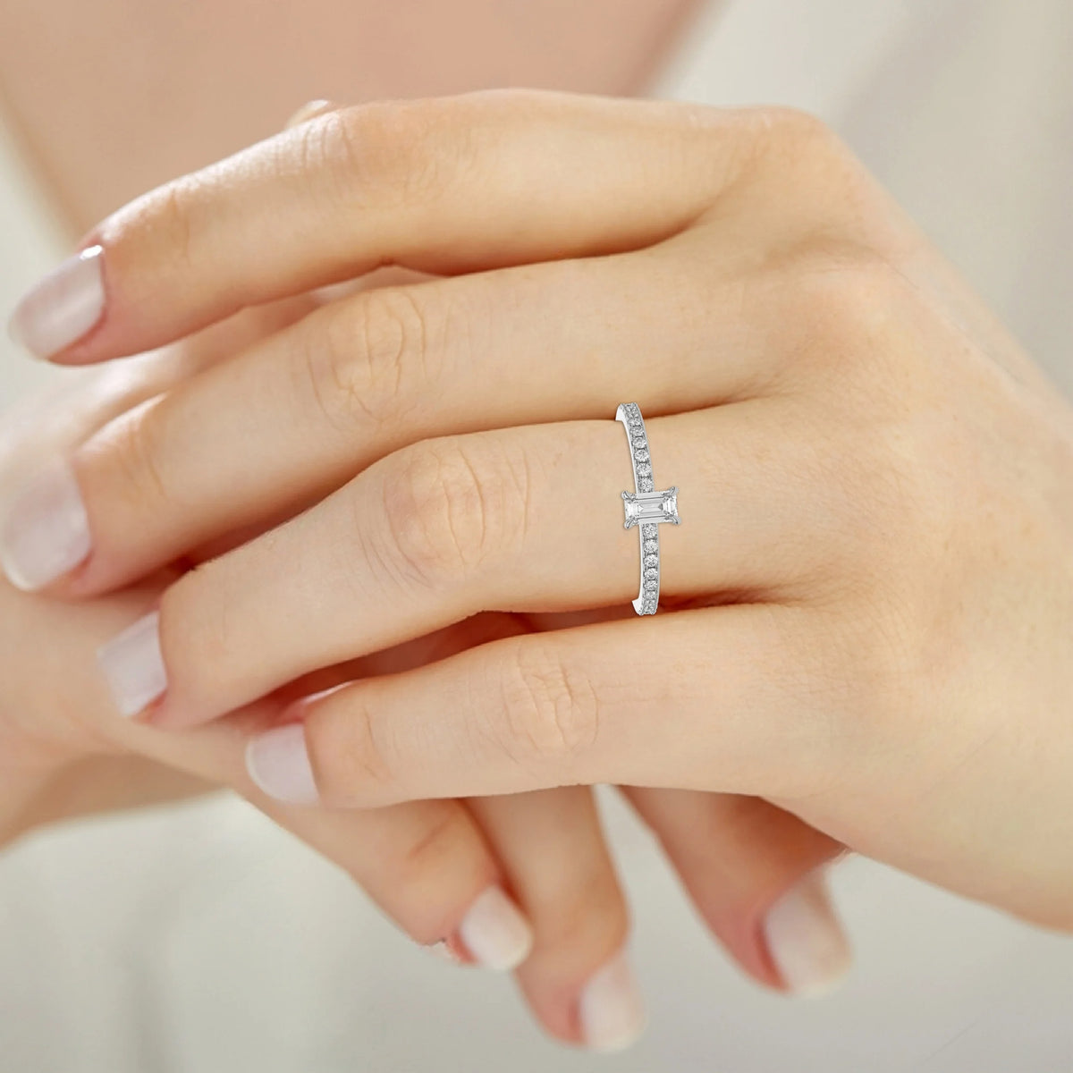 This white gold ring is made with an emerald solitaire diamond set in four-prong setting, and is complemented by a round pave diamonds band on ring finger