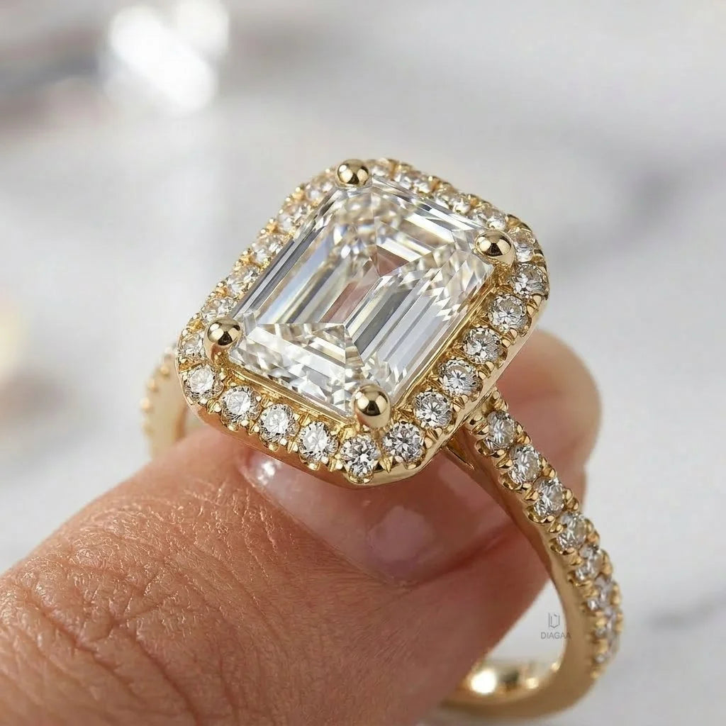 An emerald cut diamond engagement ring with a brilliant diamond halo and a pavé diamond band set in 14k yellow gold, held up closely on a finger.