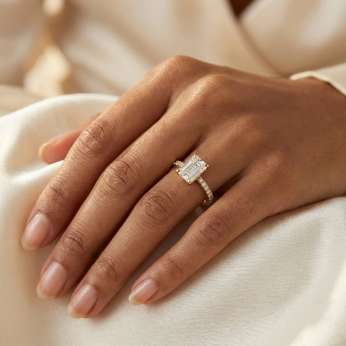 Close-up detail of a woman's hand wearing a stunning emerald cut diamond ring with a yellow gold pave band.