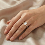 Emerald cut diamond engagement ring featuring a minimalist four-prong setting and a sparkling yellow gold pavé band on a finger.