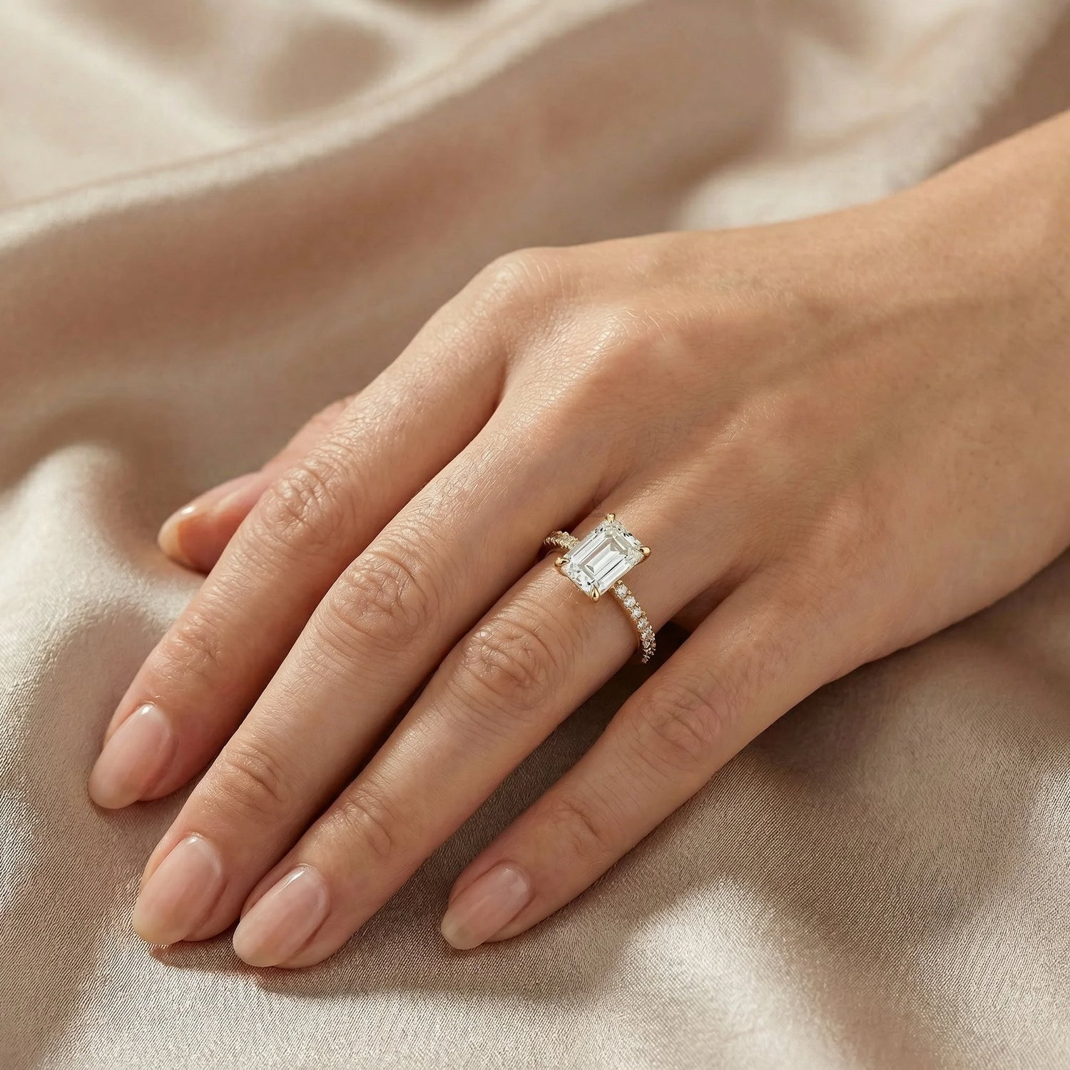 Emerald cut diamond engagement ring featuring a minimalist four-prong setting and a sparkling yellow gold pavé band on a finger.