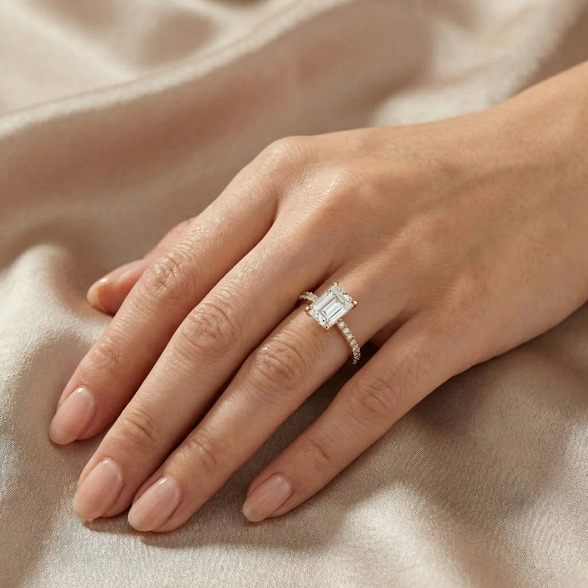 Emerald cut diamond engagement ring featuring a minimalist four-prong setting and a sparkling yellow gold pavé band on a finger.