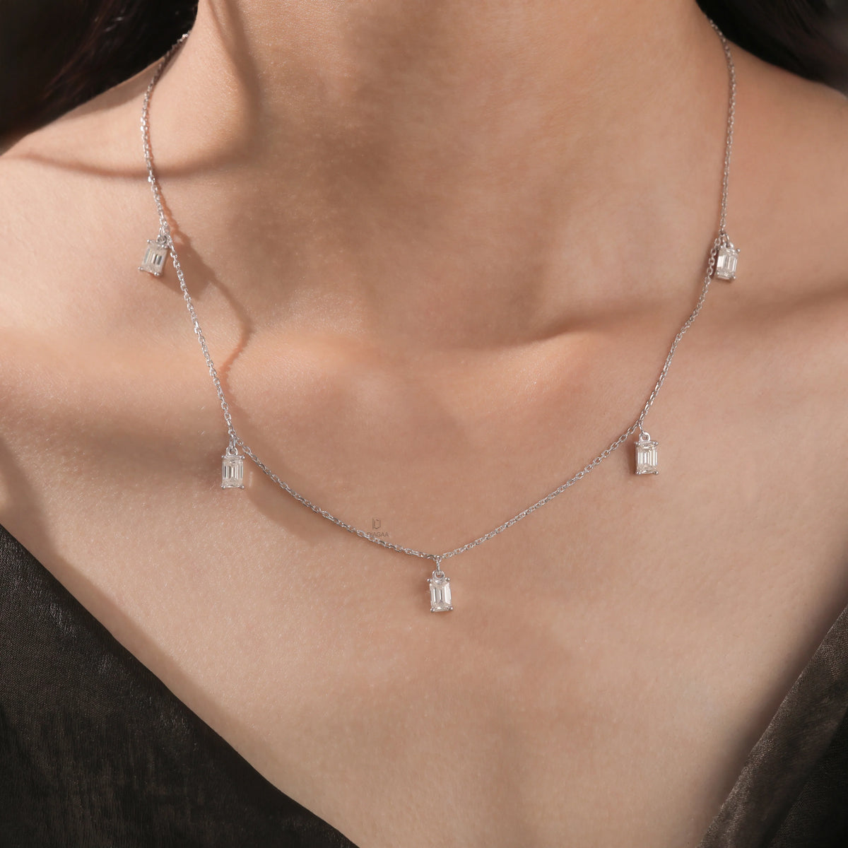 Model wearing a white gold Emerald diamond Dangling necklace featuring prong-set emerald-cut diamond charms along a fine chain.