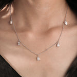 Model wearing a yellow gold Emerald diamond Dangling necklace featuring prong-set emerald-cut diamond charms along a fine chain.
