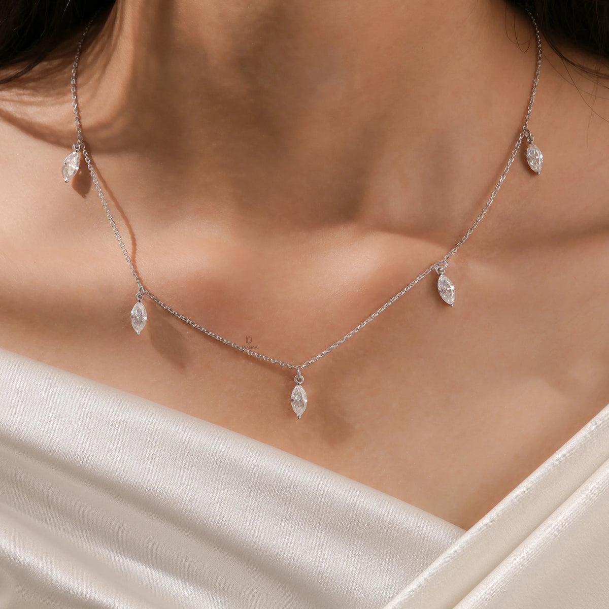 Close-up of a model's collarbone showcasing a white gold chain and a prong-set marquise diamond dangling necklace with five drop stones.