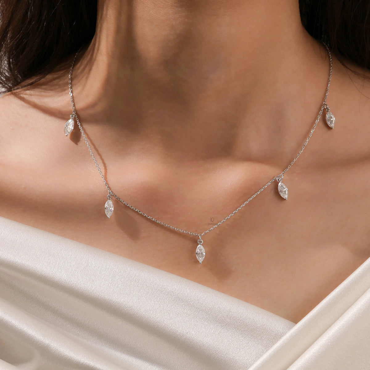 Close-up of a model's collarbone showcasing a white gold chain and a prong-set marquise diamond dangling necklace with five drop stones.