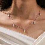 Close-up of a model's collarbone showcasing a white gold chain and a prong-set marquise diamond dangling necklace with five drop stones.