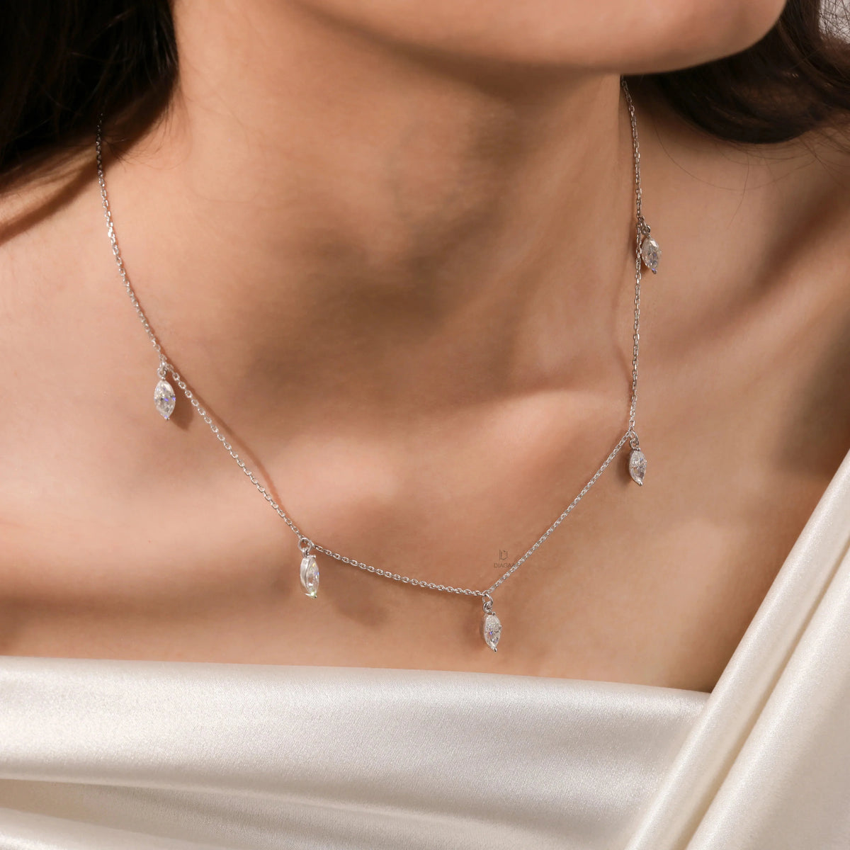 Close-up of a model's collarbone showcasing a white gold chain and a prong-set marquise diamond dangling necklace with five drop stones.