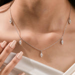 Close-up of a model's collarbone showcasing a white gold chain and a prong-set marquise diamond dangling necklace with five drop stones.