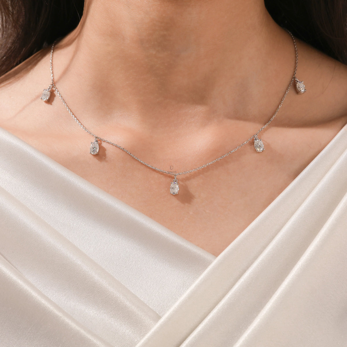 Close-up of a model's collarbone highlighting a dainty yellow gold chain and a stunning prong-set Oval diamond dangling necklace with five drop stones.