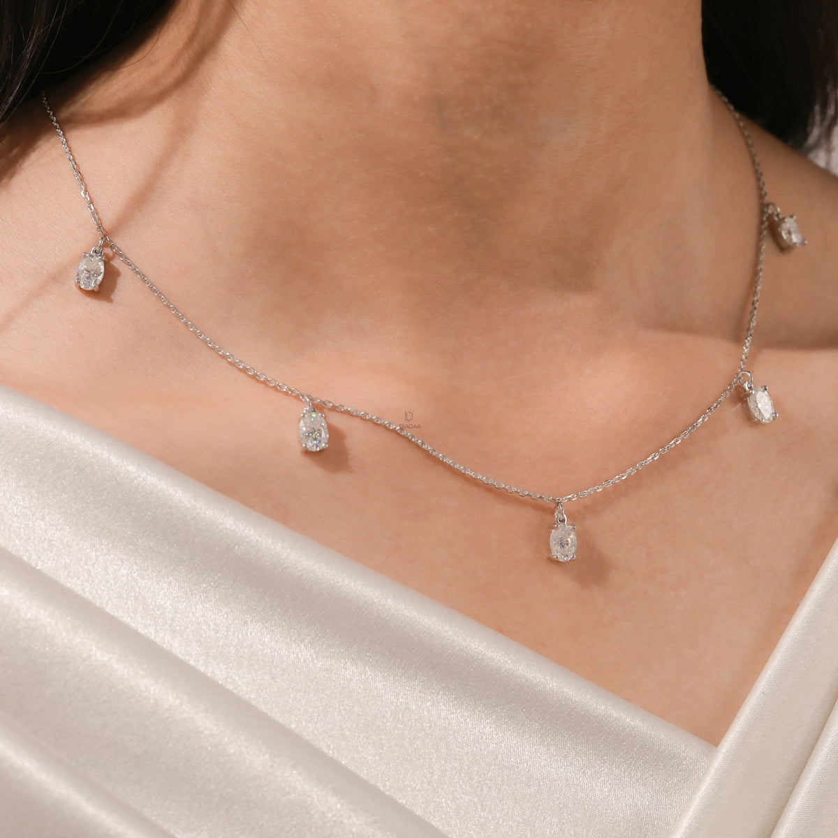 Close-up of a model's collarbone highlighting a dainty yellow gold chain and a stunning prong-set Oval diamond dangling necklace with five drop stones.
