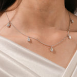 Close-up of a model's collarbone highlighting a dainty yellow gold chain and a stunning prong-set Oval diamond dangling necklace with five drop stones.