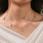 Close-up of a model's collarbone highlighting a dainty yellow gold chain and a stunning prong-set Oval diamond dangling necklace with five drop stones.