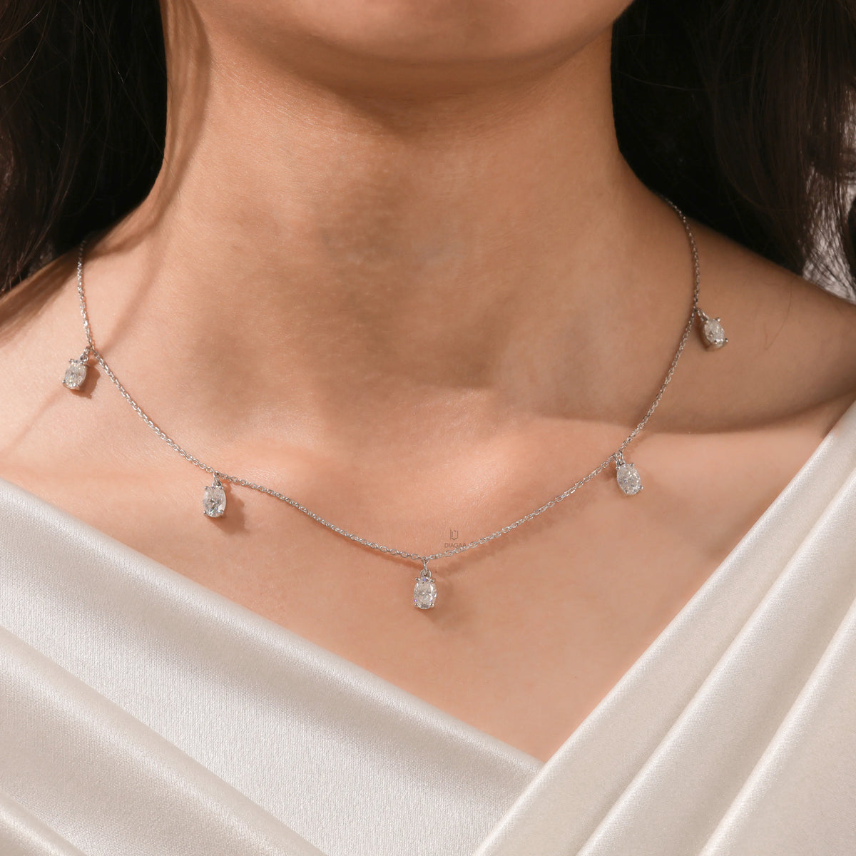 Close-up of a model's collarbone highlighting a dainty yellow gold chain and a stunning prong-set Oval diamond dangling necklace with five drop stones.