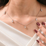 Close-up of a model's collarbone highlighting a dainty yellow gold chain and a stunning prong-set Oval diamond dangling necklace with five drop stones.