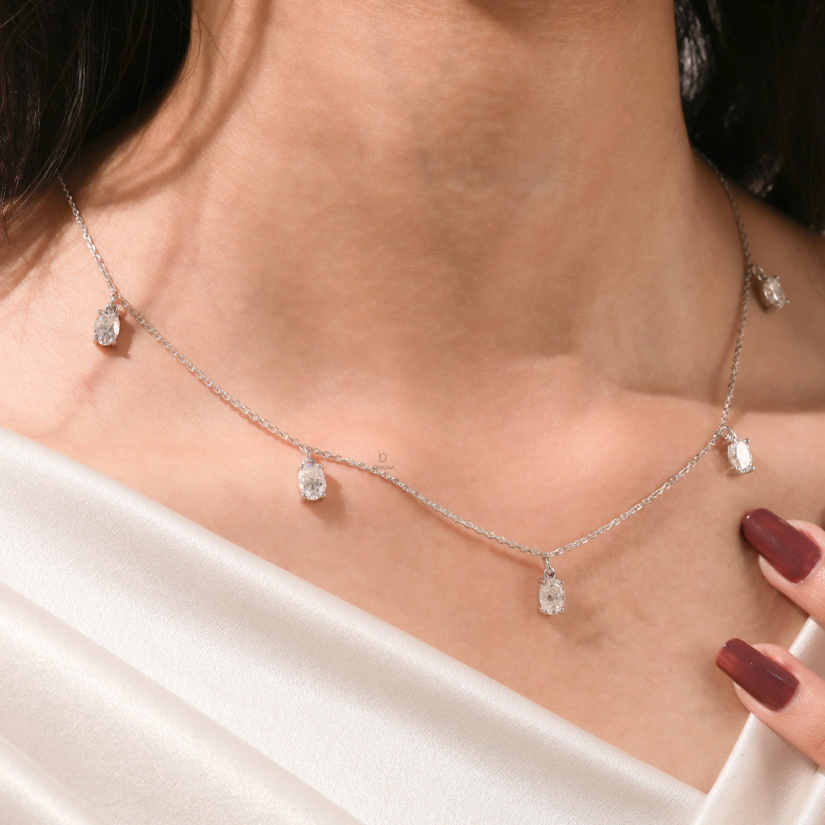 Close-up of a model's collarbone highlighting a dainty yellow gold chain and a stunning prong-set Oval diamond dangling necklace with five drop stones.