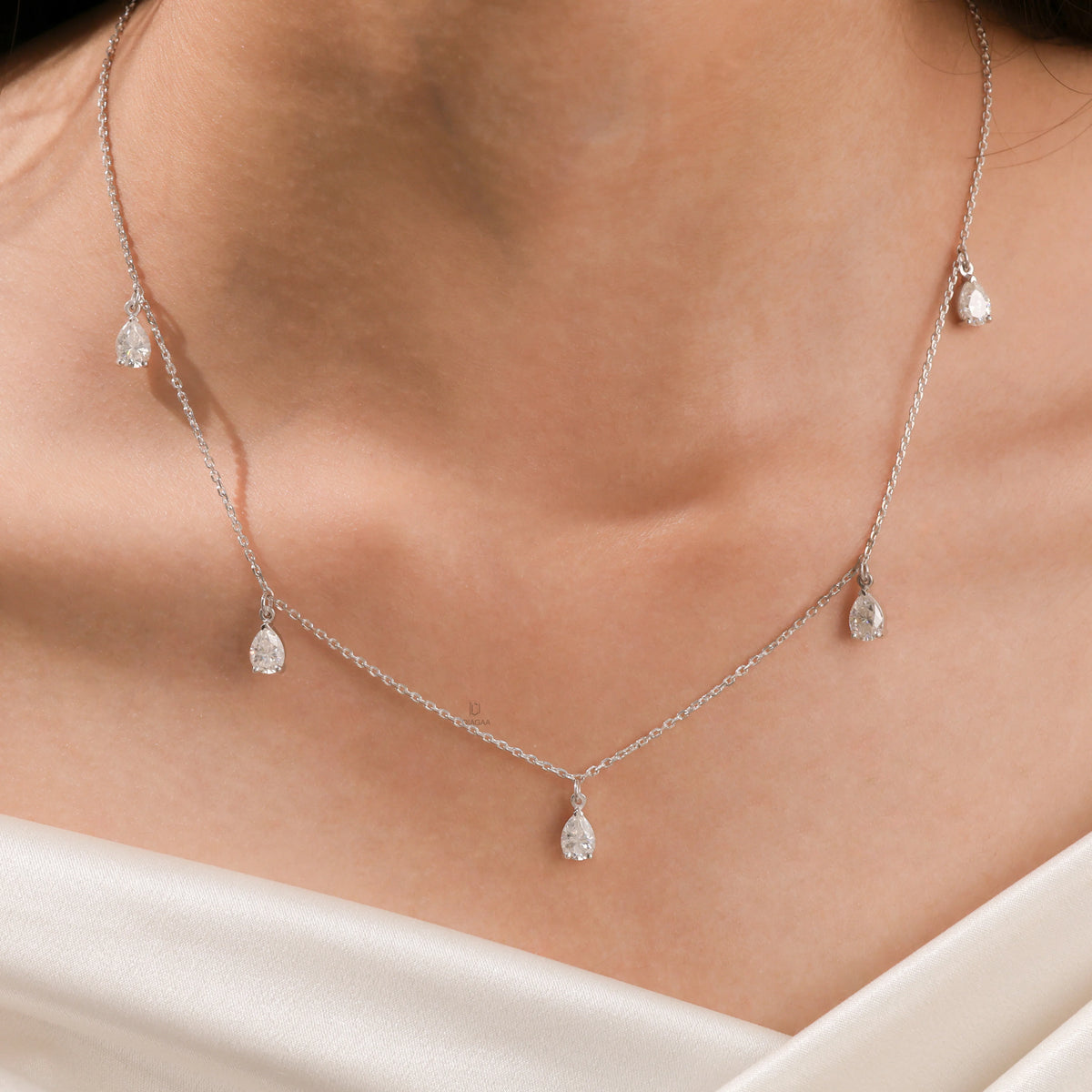 Elegant women's jewelry resting on a model's collarbone, featuring a five-stone prong-set pear diamond dangling necklace crafted in yellow gold.