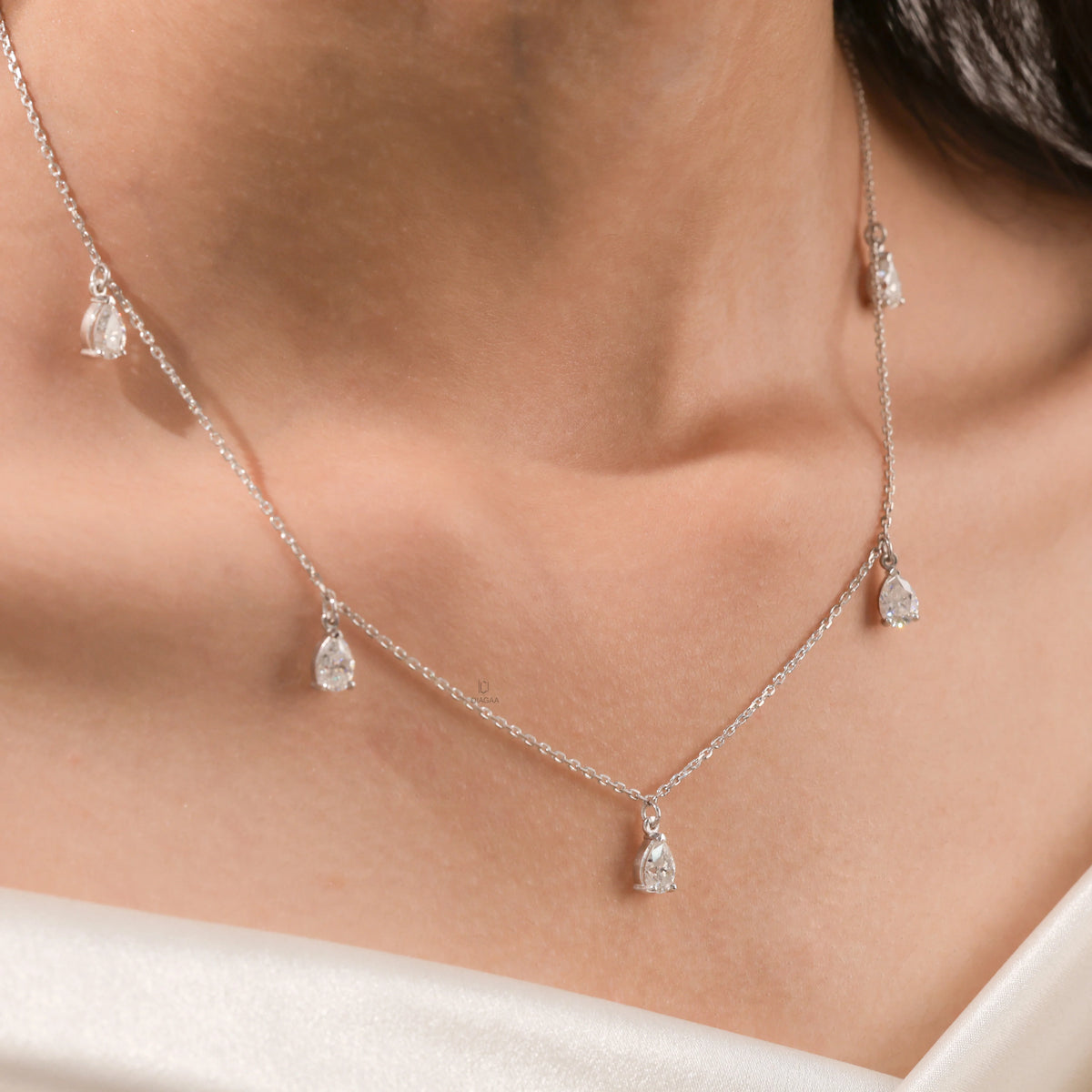 Elegant women's jewelry resting on a model's collarbone, featuring a five-stone prong-set pear diamond dangling necklace crafted in yellow gold.