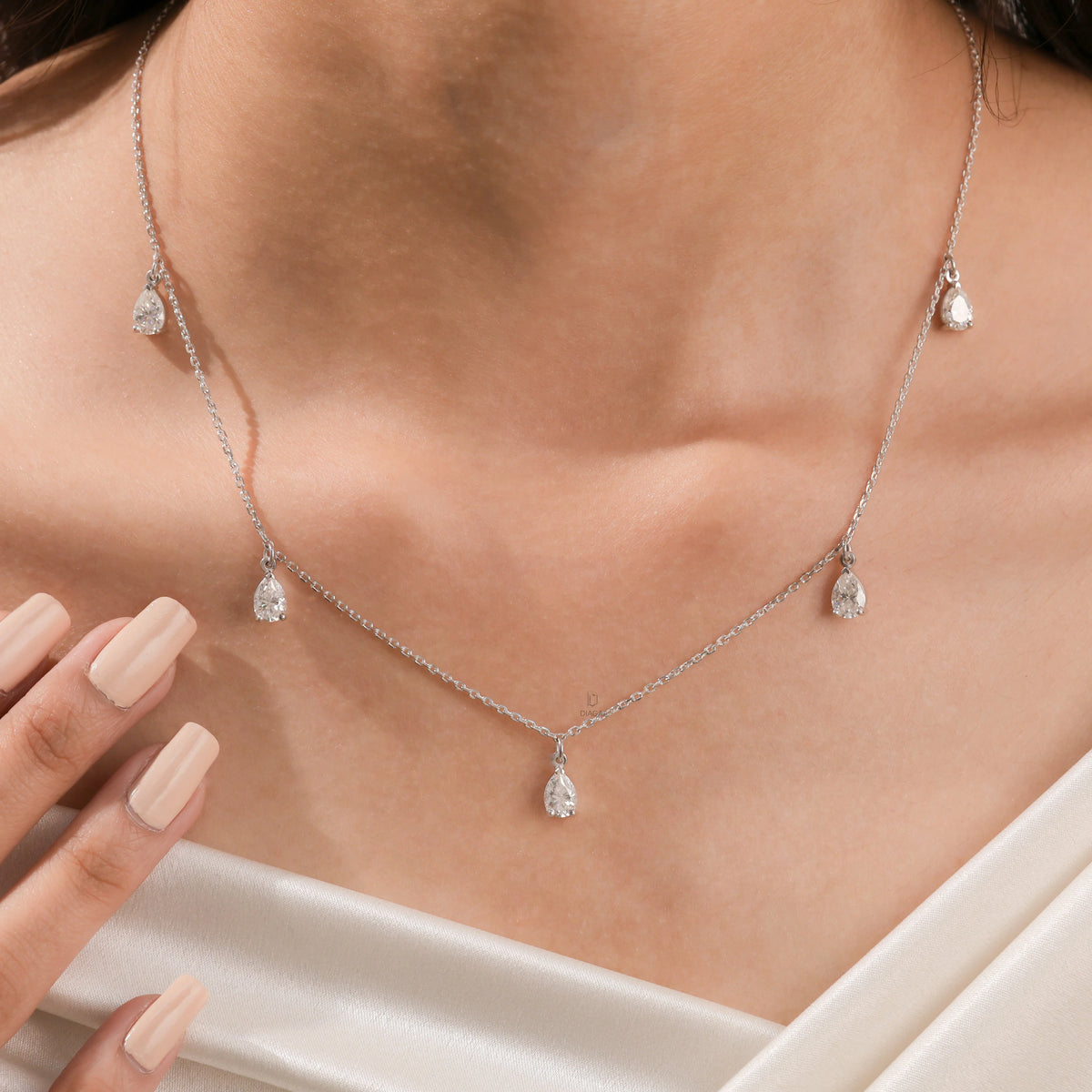 Elegant women's jewelry resting on a model's collarbone, featuring a five-stone prong-set pear diamond dangling necklace crafted in yellow gold.