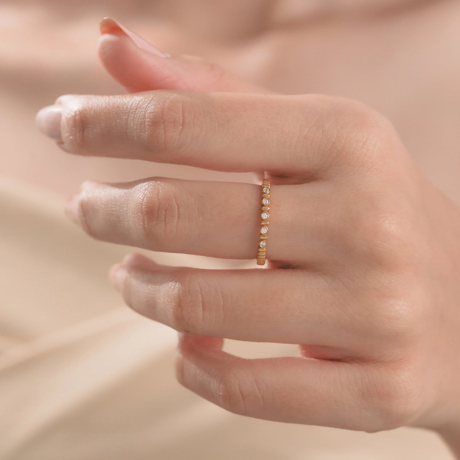 Close-up of a woman's hand wearing a textured yellow gold stackable ring with spaced round diamonds band.