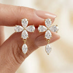 Close-up of yellow gold floral earrings featuring four pear-cut diamonds in a flower shape with a dangling marquise stone held in hand.