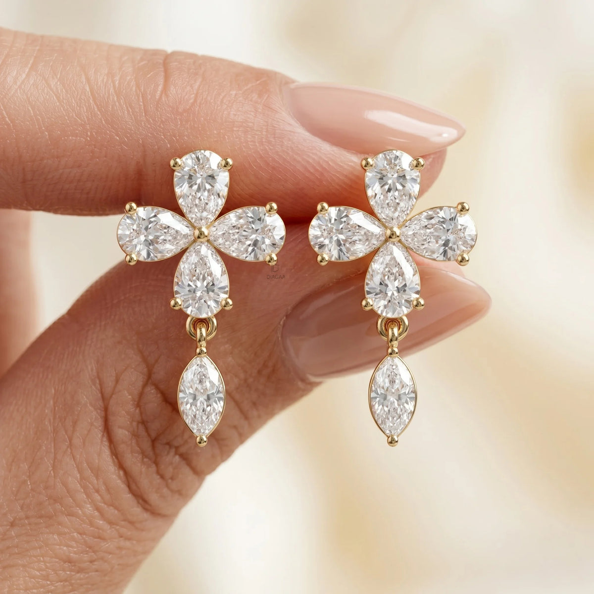 Close-up of yellow gold floral earrings featuring four pear-cut diamonds in a flower shape with a dangling marquise stone held in hand.