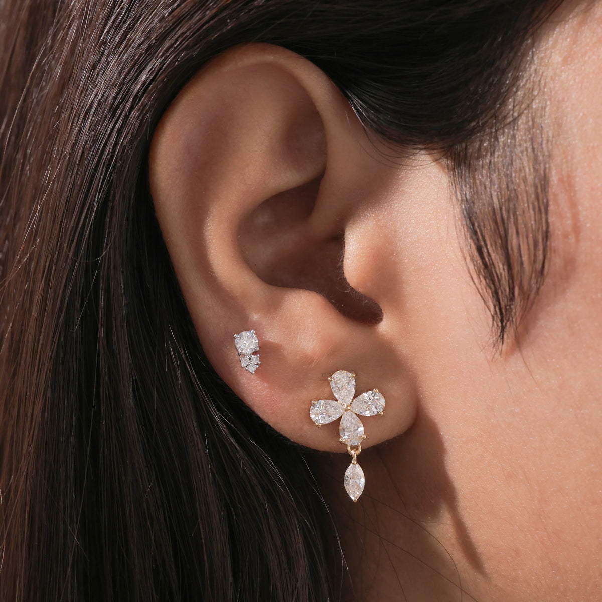 Yellow gold pear diamond flower earring with a dangling marquise drop stud on a model's ear lobe.