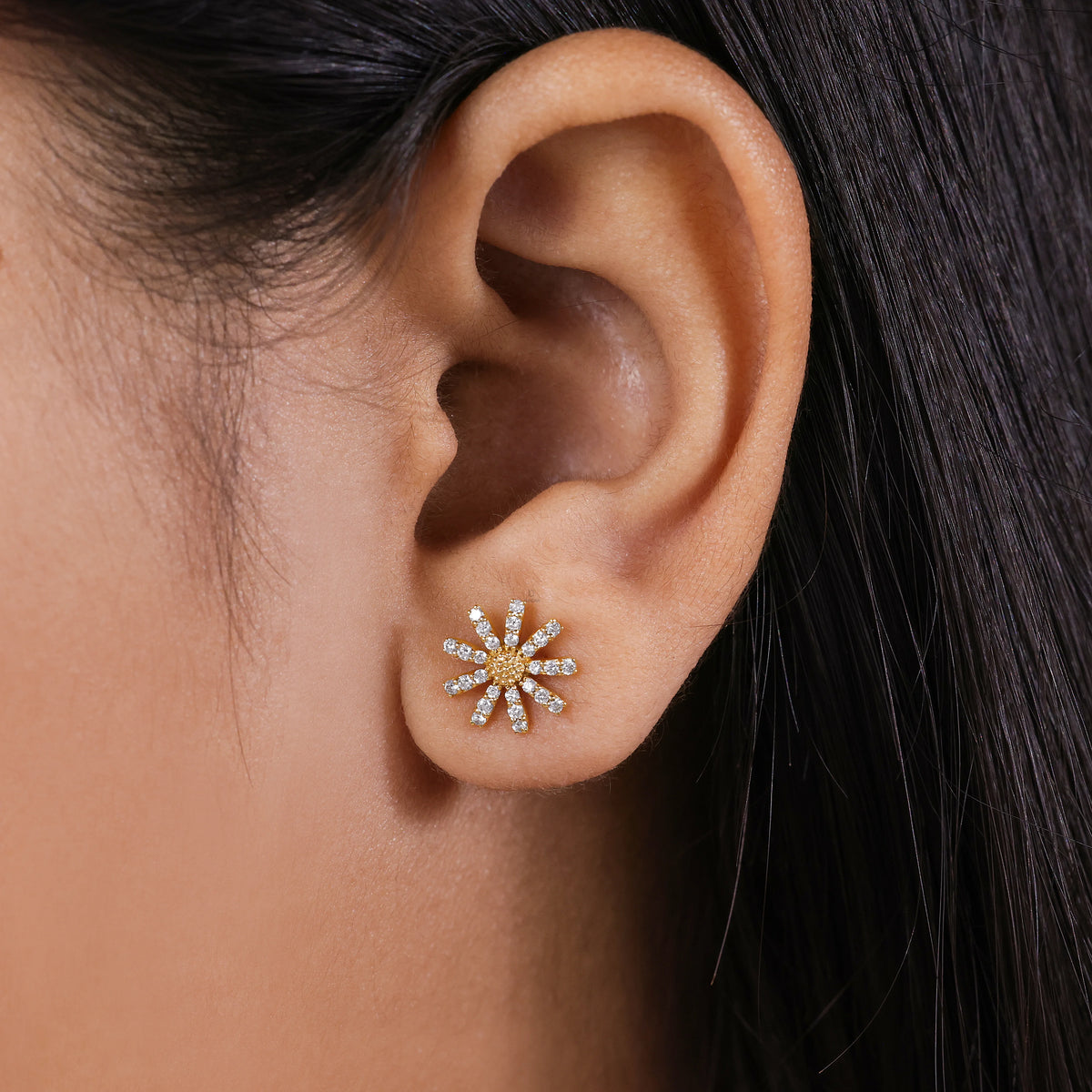 Close-up of a model wearing yellow gold flower stud earrings, featuring a sparkling diamond daisy design on the earlobe earring.