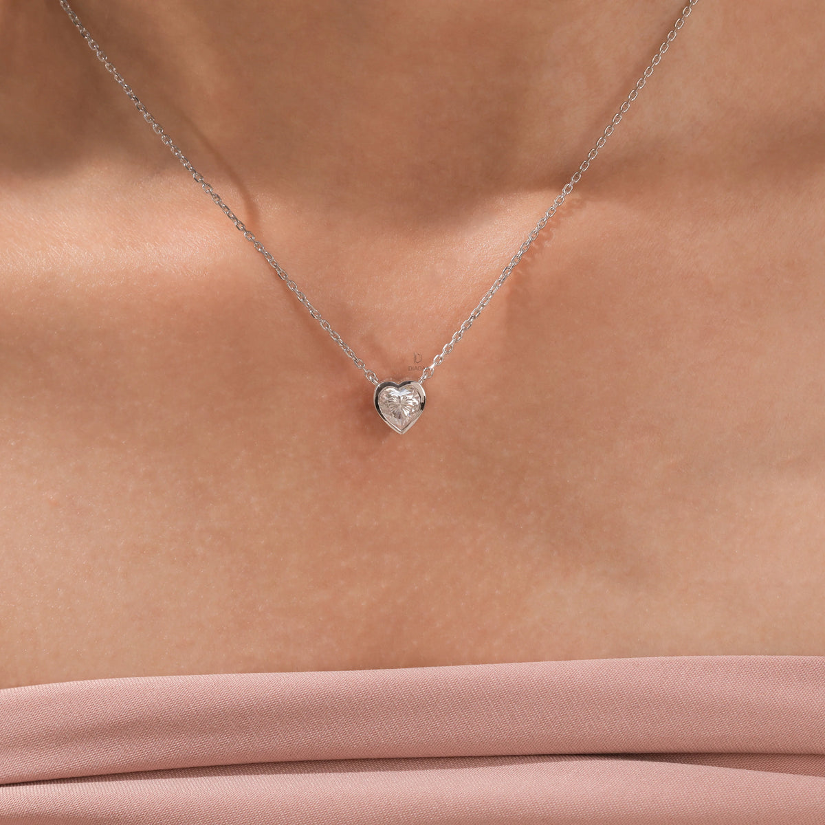 Model wearing a delicate bezel-set heart diamond necklace in white gold, featuring a brilliant heart-cut stone on a fine gold chain.
