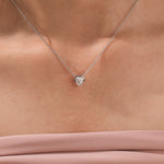 Model wearing a delicate bezel-set heart diamond necklace in white gold, featuring a brilliant heart-cut stone on a fine gold chain.