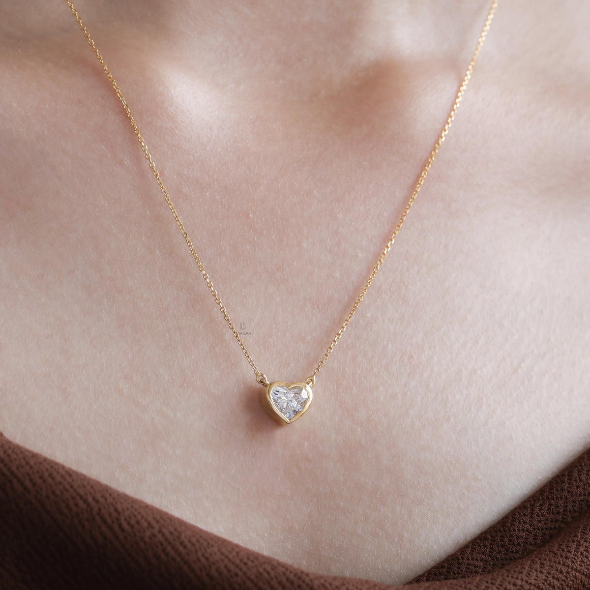 Model wearing a delicate bezel-set heart diamond necklace in yellow gold, featuring a brilliant heart-cut stone on a fine gold chain.