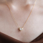 Model wearing a delicate bezel-set heart diamond necklace in yellow gold, featuring a brilliant heart-cut stone on a fine gold chain.