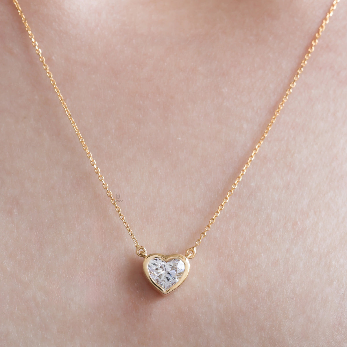 Model wearing a delicate bezel-set heart diamond necklace in yellow gold, featuring a brilliant heart-cut stone on a fine gold chain.