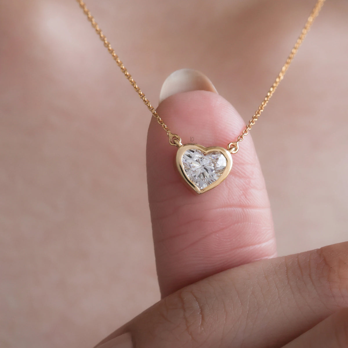 Model wearing a delicate bezel-set heart diamond necklace in yellow gold, featuring a brilliant heart-cut stone on a fine gold chain.