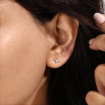 A close-up view of a woman wearing a delicate marquise diamond stud earring set in solid 14K yellow gold, showcasing a three-stone floral cluster design that is securely prong-set on the earlobe.