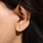 A close-up view of a woman wearing a delicate marquise diamond stud earring set in solid 18K yellow gold, showcasing a three-stone floral cluster design that is securely prong-set on the earlobe