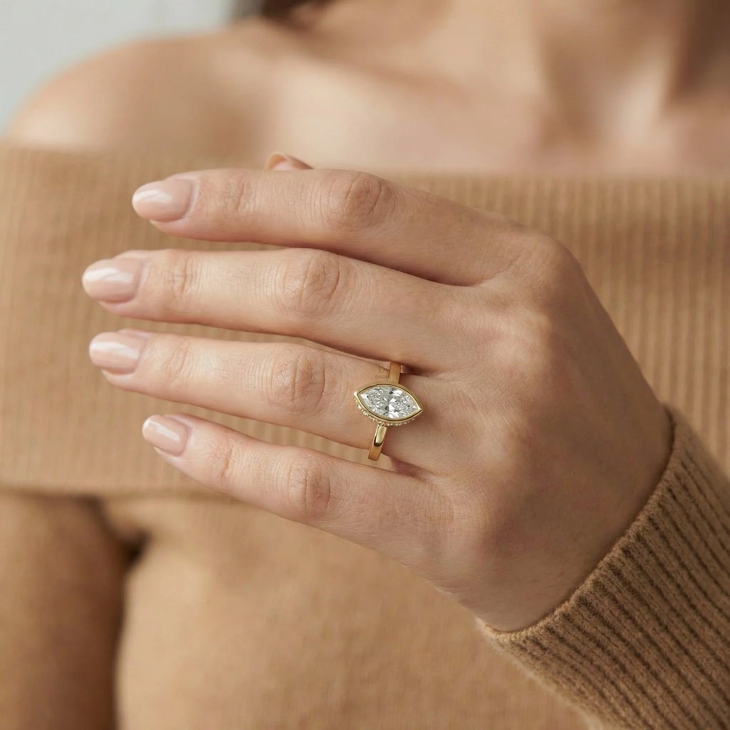 Yellow gold east-west marquise diamond ring with a pavé set, worn on a hand against a brown sweater.