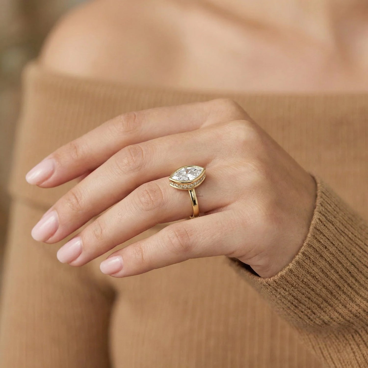 Marquise cut diamond engagement ring with a yellow gold bezel setting worn on a woman's hand.