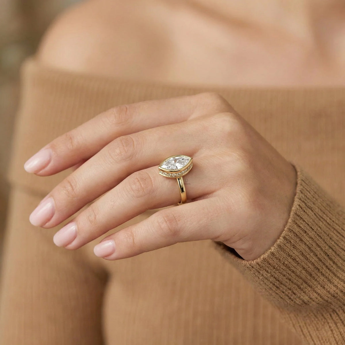 Marquise cut diamond engagement ring with a yellow gold bezel setting worn on a woman's hand.
