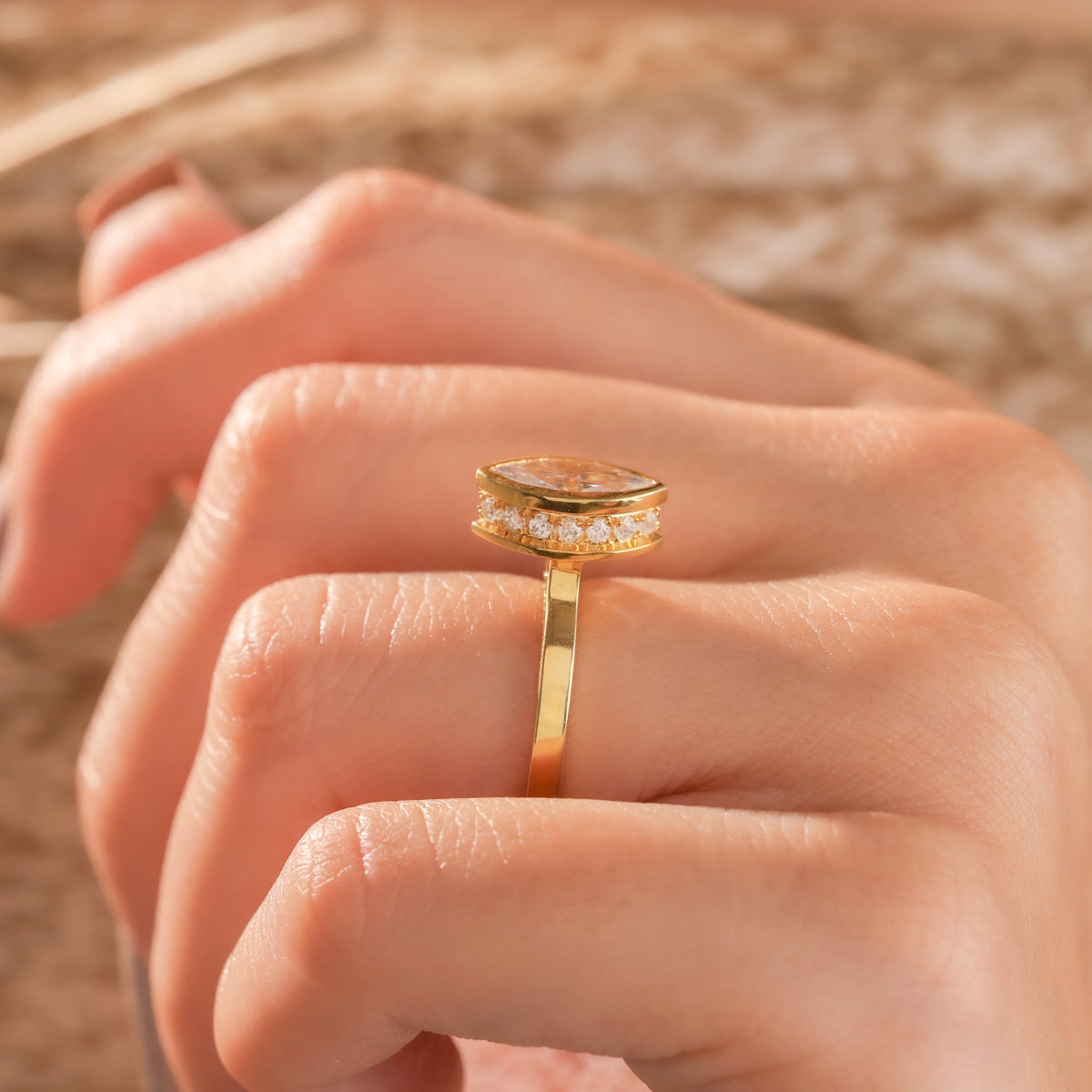 Close-up Side view of a marquise cut diamond ring with a yellow gold bezel setting worn on a finger.