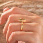 Close-up Side view of a marquise cut diamond ring with a yellow gold bezel setting worn on a finger.