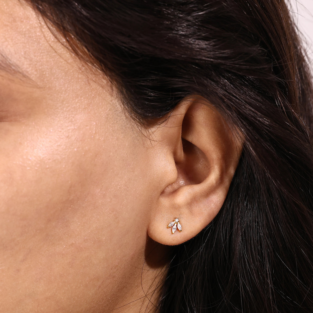 Close-up of a woman wearing a delicate yellow gold stud earring featuring three marquise-cut diamonds arranged in a floral cluster.