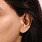 Close-up of a woman wearing a delicate yellow gold stud earring featuring three marquise-cut diamonds arranged in a floral cluster.