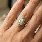 A close-up of a hand wearing a yellow gold engagement ring featuring a stunning marquise diamond Solitaire ring with round diamond halo set ring 