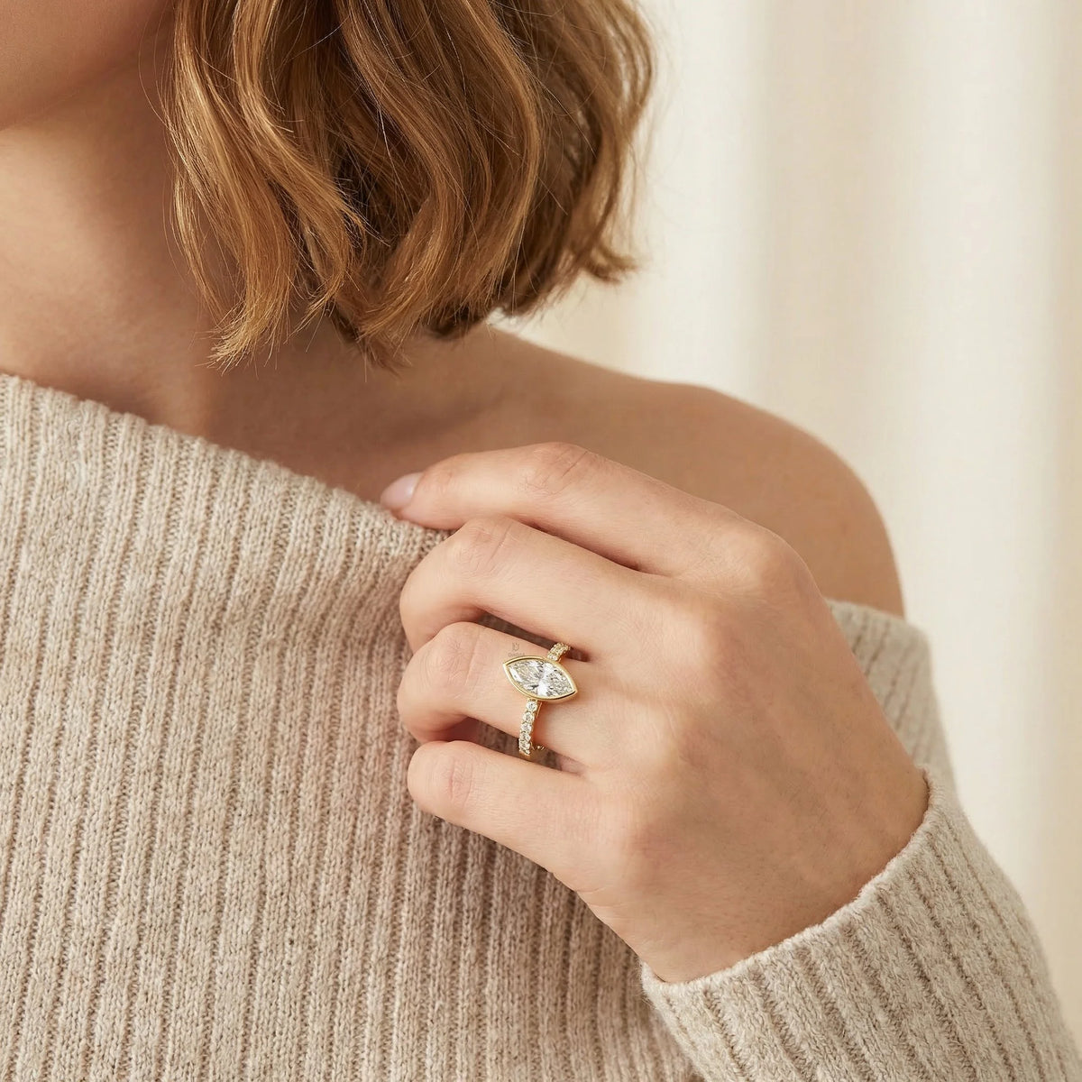 Modern yellow gold bezel solitaire ring with an east-west marquise diamond and a sparkling diamond accented band, displayed gracefully on a hand for an elegant bridal look.