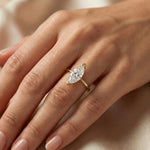 Solitaire marquise diamond engagement ring in a yellow gold v-prong setting, worn on a ring finger against a neutral satin backdrop.